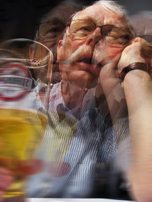 AlcoholicA blurry, triple vision of an older man sitting, open mouthed and holding a glass of beer.