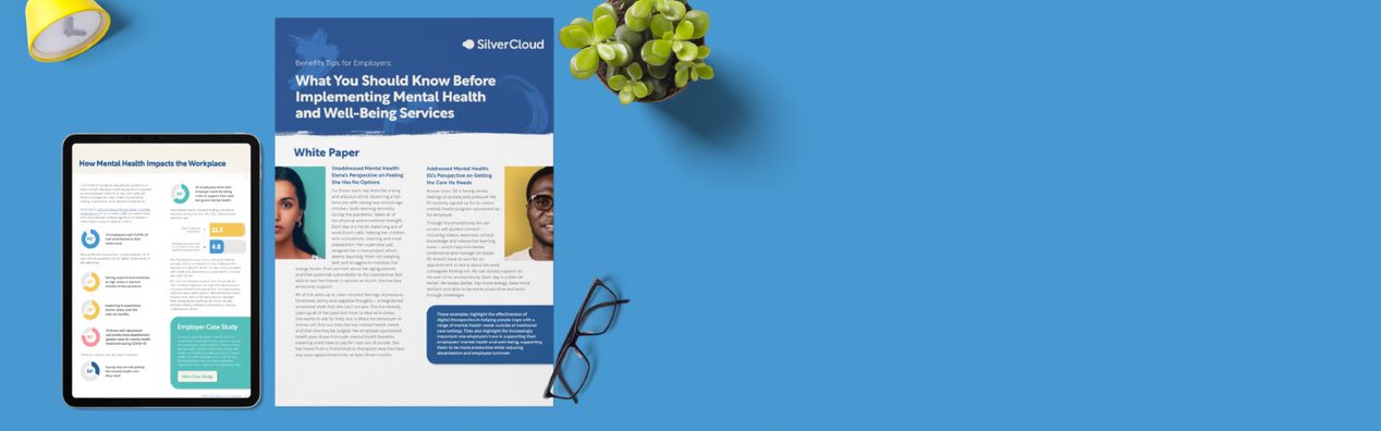A printed whitepaper, a tablet showing another whitepaper, glasses, a small potted plant and a yellow clock.