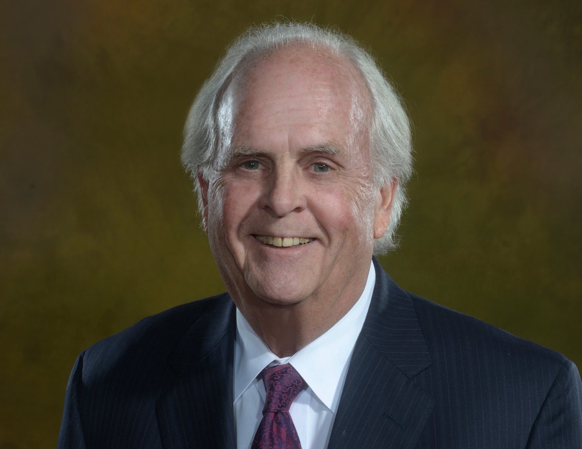 Dr. David Barlow who is wearing a dark blue, pin striped suit, a red and blue tie and is smiling.