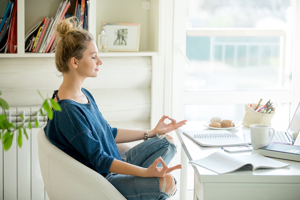 A woman sitting at a desk in her home office, meditating.