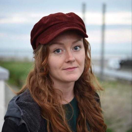 Rebecca Wogan, who is a research assistant at SilverCloud Health, and is wearing a black coat, a green shirt and dark red hat.