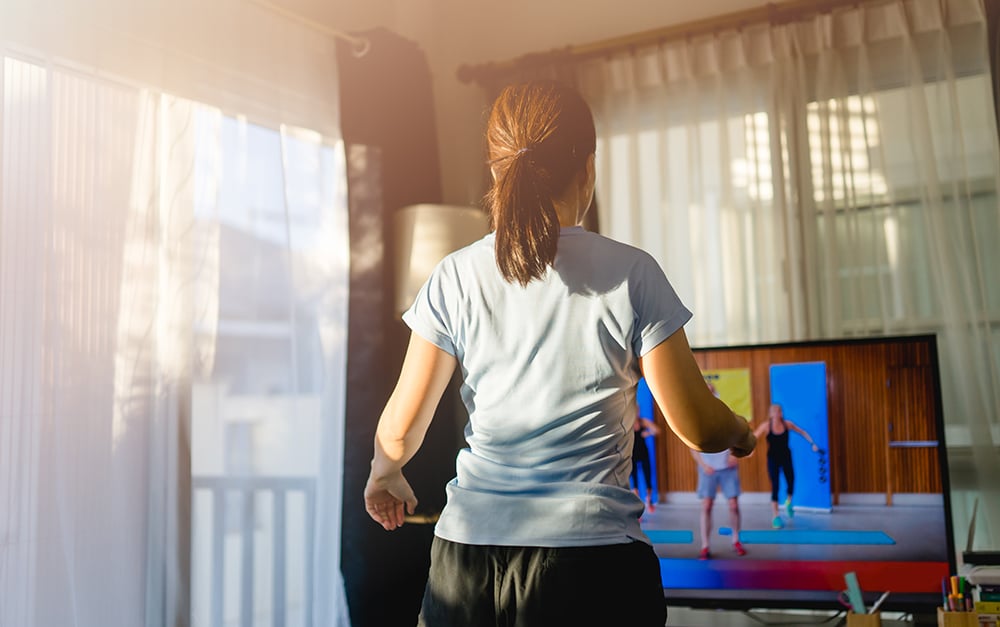 A woman exercising in her home to an exercise video.