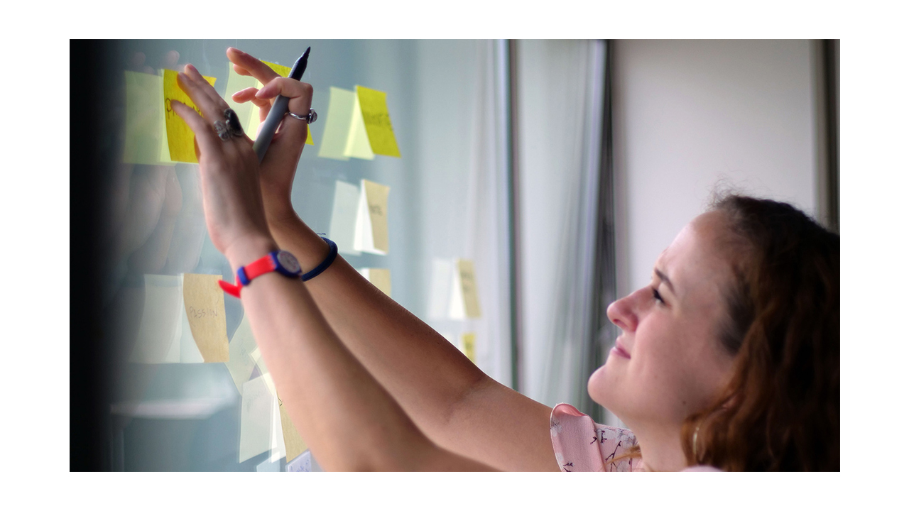 A woman with a Sharpie in her hand, putting yellow post-its on a window.